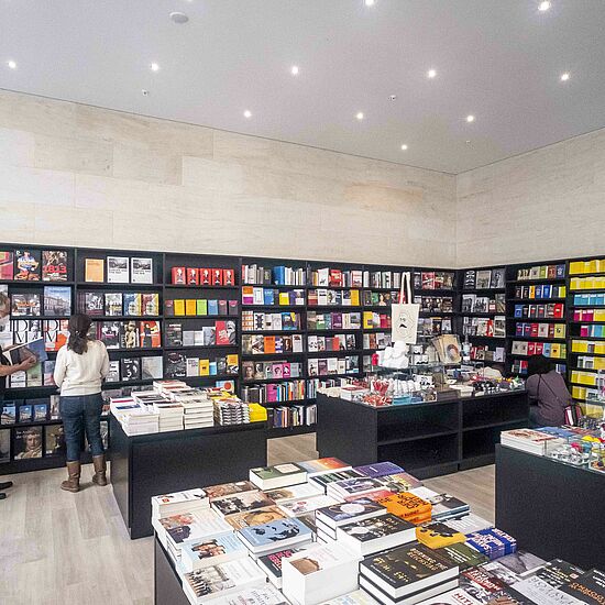 Zwei Personen stehen vor dem Bücherregal im Shop des Museums und lesen in Büchern.