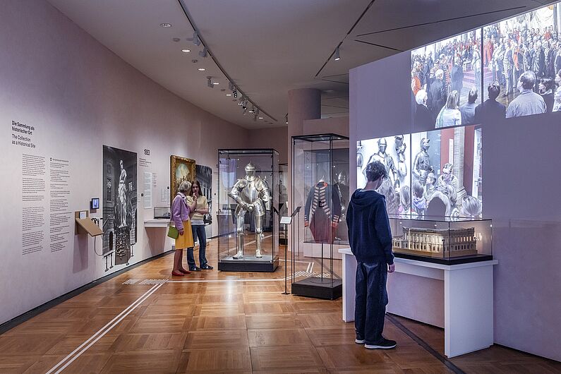 In der Ausstellung „Objekte. Geschichte. Geschichten. Blick in die Sammlung” Menschen stehen in einer Ausstellung