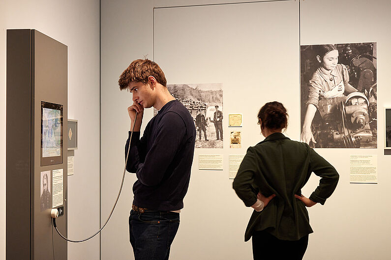 In der Ausstellung „Umstrittene Verwandtschaft. Koloniale und nationalsozialistische Gewalt” Menschen stehen in einer Ausstellung