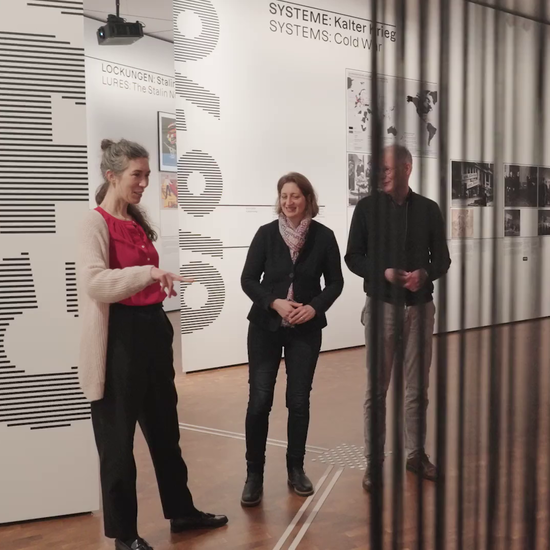 Drei Leute stehen vor einer Ausstellungswand und reden miteinander.