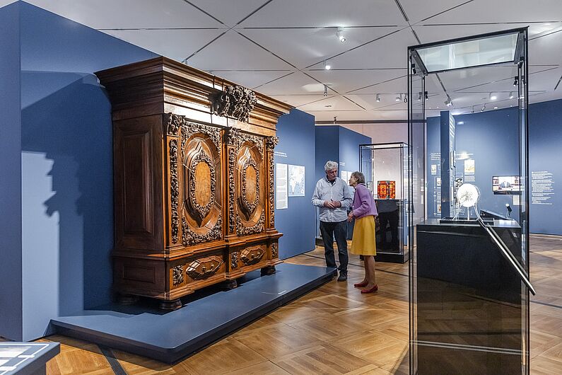 In der Ausstellung „Objekte. Geschichte. Geschichten. Blick in die Sammlung” Menschen stehen in einer Ausstellung