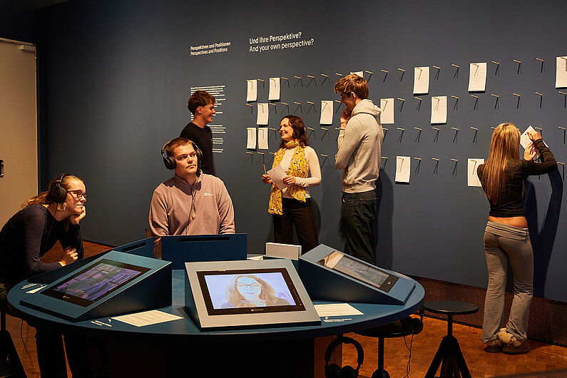 In der Ausstellung „Umstrittene Verwandtschaft. Koloniale und nationalsozialistische Gewalt” Menschen stehen in einer Ausstellung