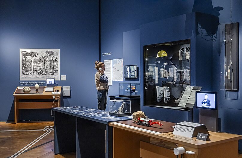 In der Ausstellung „Objekte. Geschichte. Geschichten. Blick in die Sammlung” Menschen stehen in einer Ausstellung