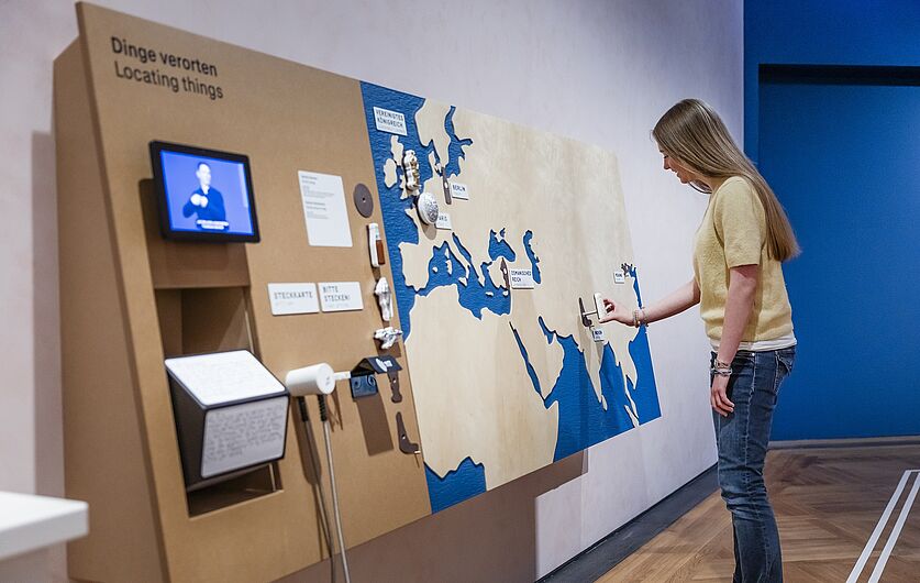 In der Ausstellung „Objekte. Geschichte. Geschichten. Blick in die Sammlung” Menschen stehen in einer Ausstellung
