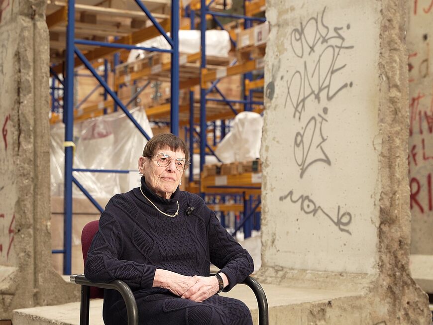 Eine Frau sitzt vor Originalteilen der Berliner Mauer in einer Halle.