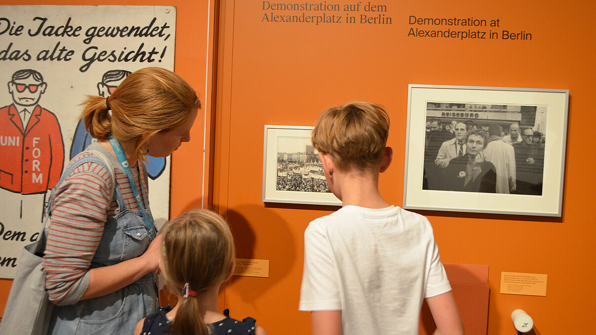 Kinderführung "Warte nicht mit deinem Mut!" Eine Frau und zwei Kinder sehen sich eine Fotographie an.