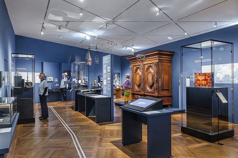 In der Ausstellung „Objekte. Geschichte. Geschichten. Blick in die Sammlung” Menschen stehen in einer Ausstellung