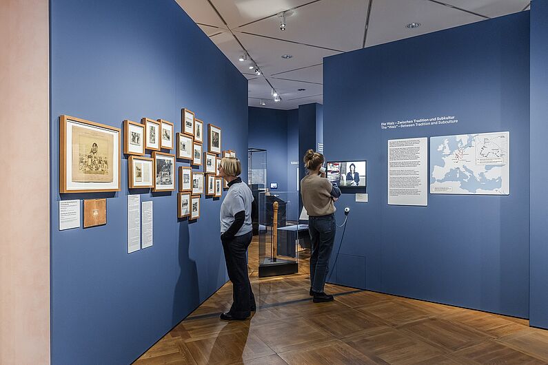 In der Ausstellung „Objekte. Geschichte. Geschichten. Blick in die Sammlung” Menschen stehen in einer Ausstellung