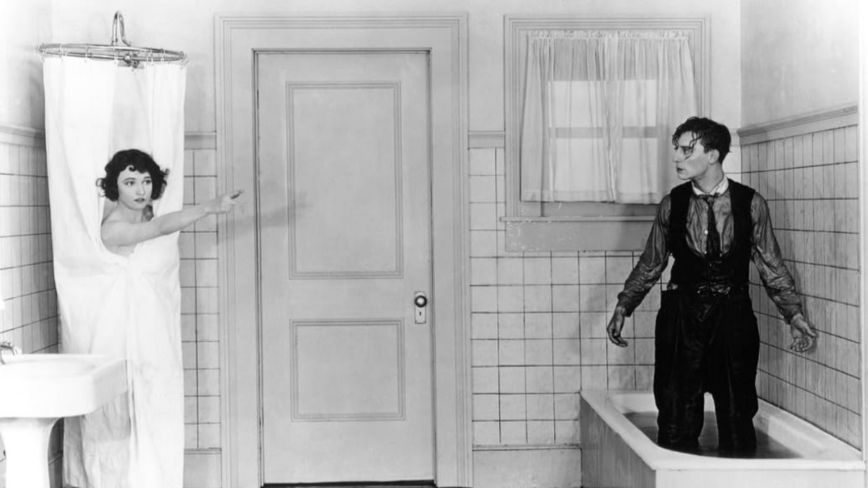 Ein Mann steht in einer Badewanne und eine Frau steht, bedenkt vom Duschvorhang, in einer Dusche.