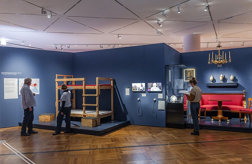 In der Ausstellung „Objekte. Geschichte. Geschichten. Blick in die Sammlung” Menschen stehen in einer Ausstellung