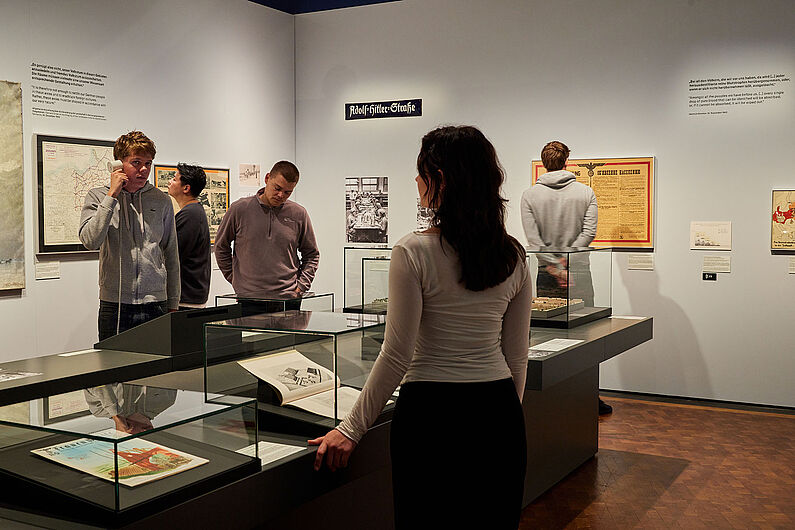 In der Ausstellung „Umstrittene Verwandtschaft. Koloniale und nationalsozialistische Gewalt” Menschen stehen in einer Ausstellung