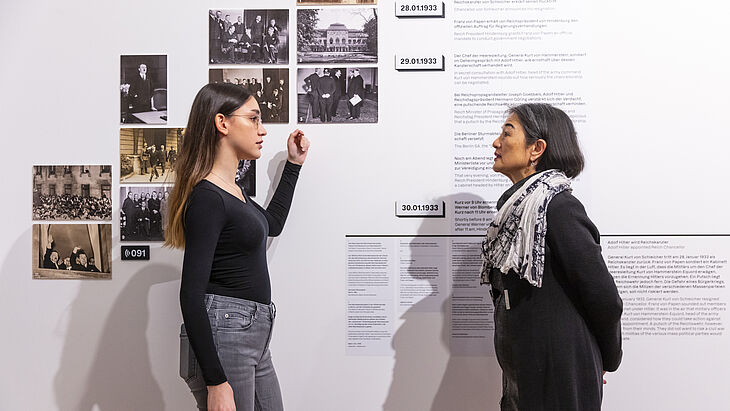 Zwei Frauen stehen vor einer Ausstellungswand und führen ein Gespräch.