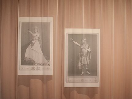 Hinter transparenten dünnen rosafarbenen Vorhängen in der Ausstellung "Richard Wagner und das deutsche Gefühl" sind zwei großformatige schwarz-weiß Fotografien zu sehen die Darsteller*innen aus den Stücken von Wagner zeigen.