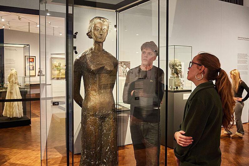 In der Ausstellung „Umstrittene Verwandtschaft. Koloniale und nationalsozialistische Gewalt” Menschen stehen in einer Ausstellung