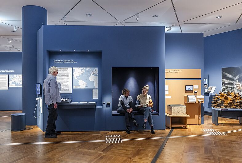 In der Ausstellung „Objekte. Geschichte. Geschichten. Blick in die Sammlung” Menschen stehen in einer Ausstellung