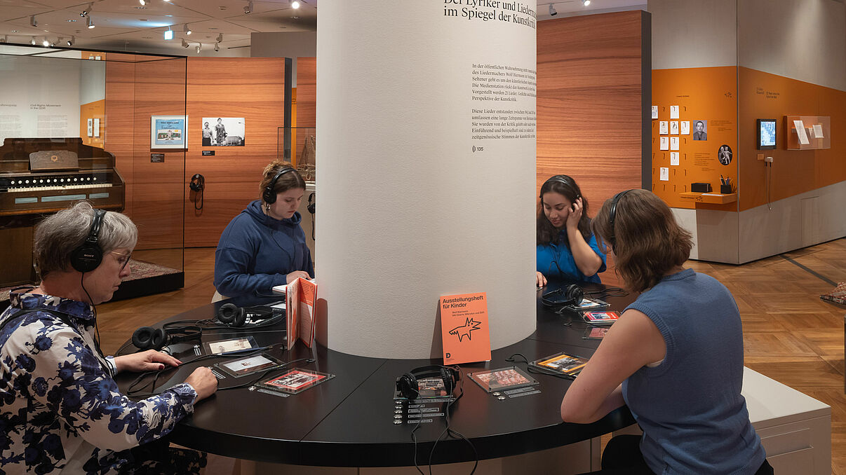 Vier Frauen sitzen an einem Tisch und hören sich etwas an.