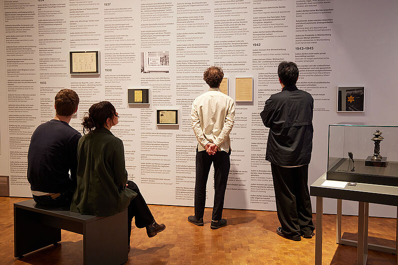In der Ausstellung „Umstrittene Verwandtschaft. Koloniale und nationalsozialistische Gewalt” Menschen stehen in einer Ausstellung