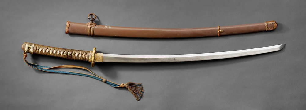 The photo shows a Shin Gunto, a modern military sword used by the Japanese Army during World War II, along with its scabbard. The blade is curved, and the sword has a simple design.