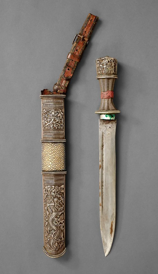 The photo shows a Tibetan dughti, that is, a culturally significant dagger with a broad blade and an ornate handle. Below it lies the equally richly decorated dagger sheath.